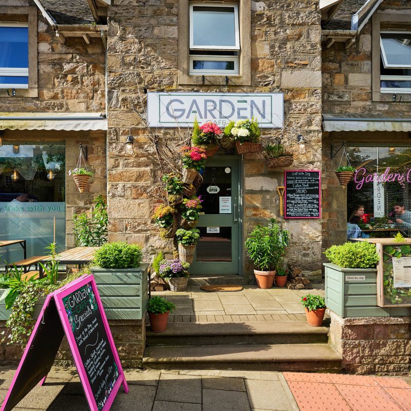 A brick building with a floral arrangement over the door and a white sign which reads 'Garden Cafe.'