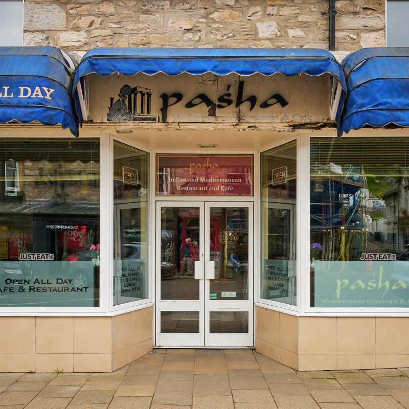 A brick building with blue accents and a black sign which reads Pasha.