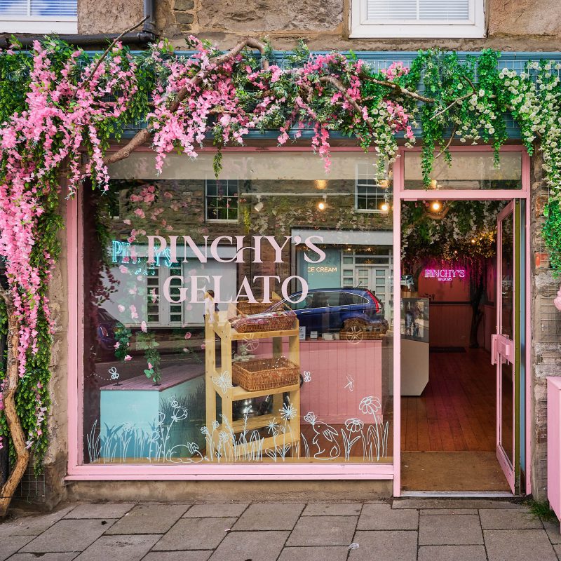 A pink building with large windows. There are pink and white flowers wrapping around the shop.