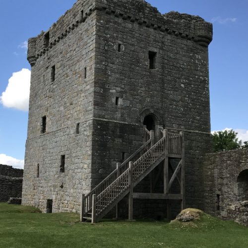 Old, stone turreted building with small narrow holes for windows, under a blue sky.