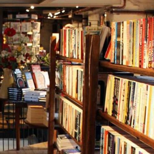 Bookcases filled with books with a railing and a table with a vase of flowers on it and seating behind