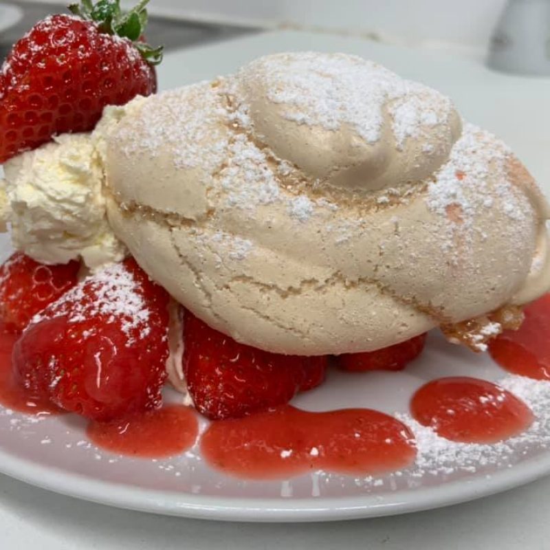 Meringue on a white plate with fresh cream and strawberries