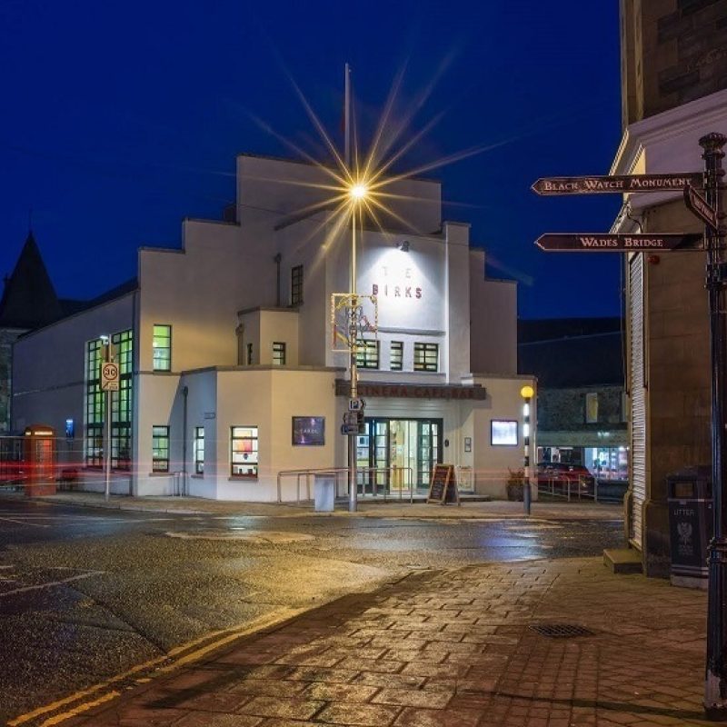 Art Deco white building at night with a cobbled street and an old fashioned cast iron street sign