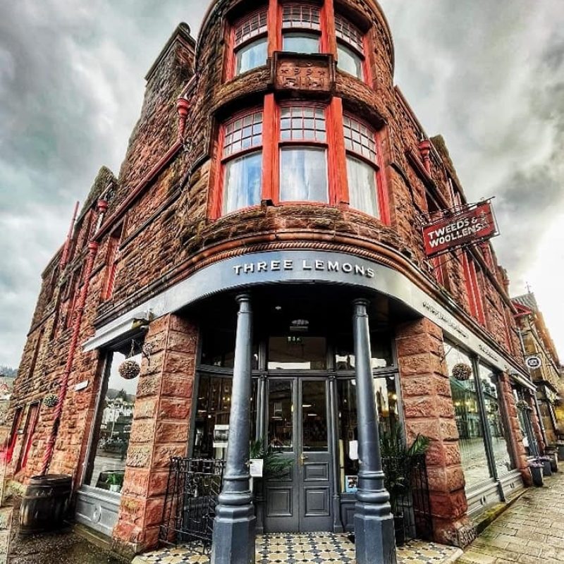 Red sandstone building with black columns at entrance and sign above on trim saying Three Lemons