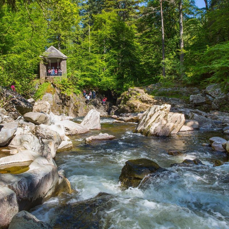 Small stone building set in a green forest overlooking water  tumbling over rocks