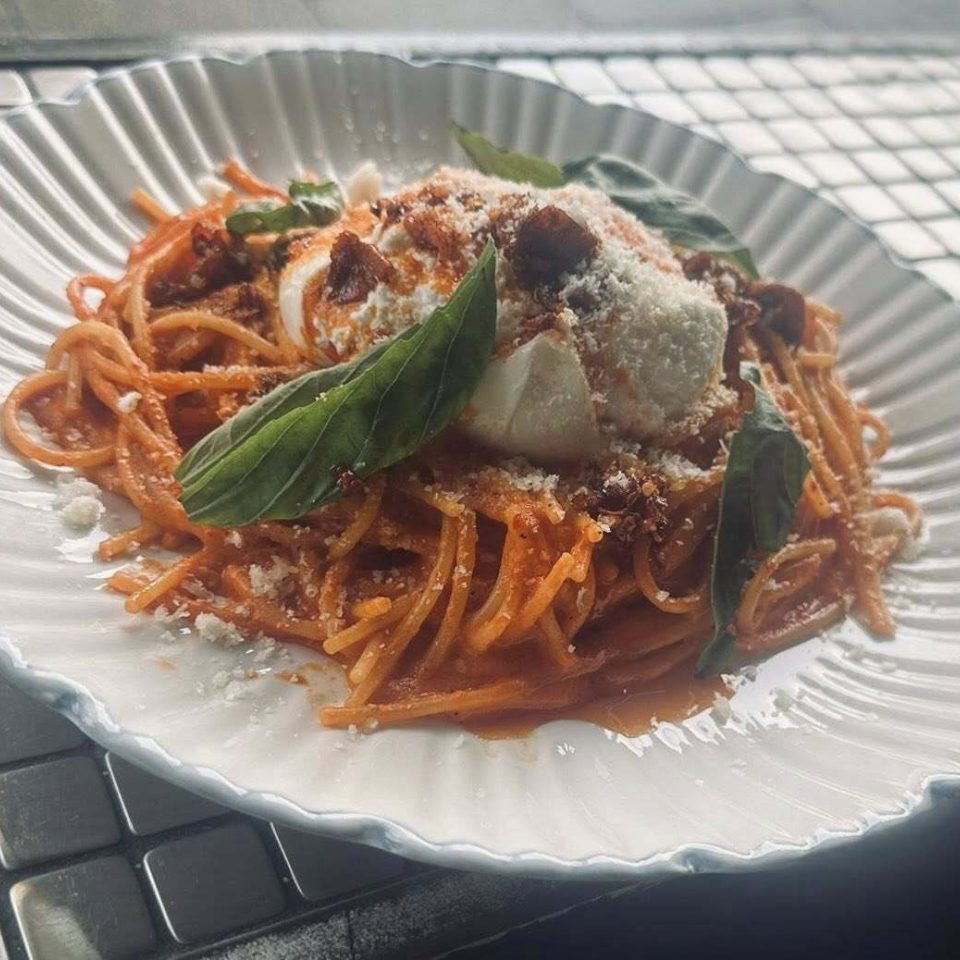 White large bowl with spaghetti in a tomato sauce and mozzarella, basil and sundried tomatoes on top
