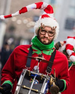 Man with red and white stripey hat, christmas outfit and big black drum.