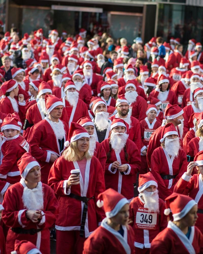 Lots of smiling people wearing Santa suits getting ready to race outside
