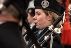 A woman playing the bagpipes wearing a blue shirt and a black jacket