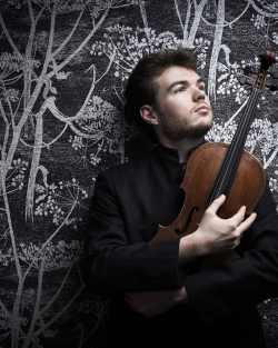 A man wearing all black holding a violin looking longingly into the distance.