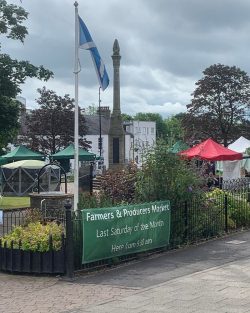 Open park area with coloured outdoor umbrellas and sign for Blairgowrie Farmers' and Producers Market
