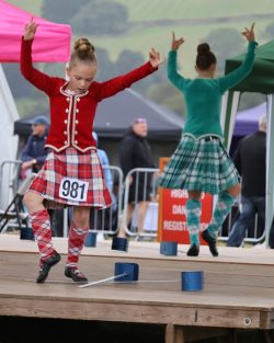 Two girls wearing tartan skirts highland dancing on a stage
