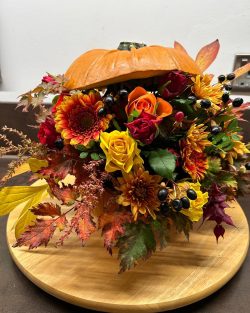 A pumpkin which is cut in half with an arrangement of orange and red flowers inside.