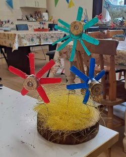 Handmade flowers of different colours standing in a wooden base with shredded tissue paper.