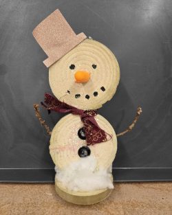 An image of a handmade snowman made of yarn circles, with buttons, sticks and a scarf for accessories.