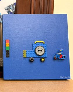 Blue canvas with a blue lego car and lego man on a blue motorcycle on it.