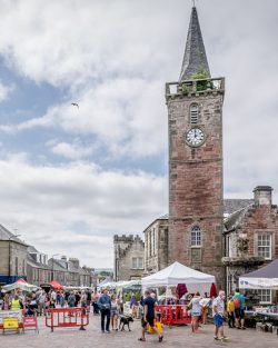 Cloudy blue sky with large old clock tower and market stalls in the foreground.