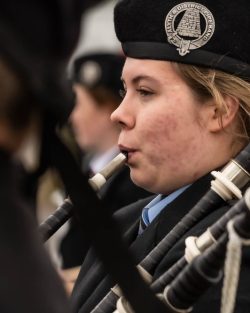 A woman playing the bagpipes wearing a blue shirt and a black jacket