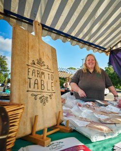 Wooden Farm to Table sign and smiling woman at market stall