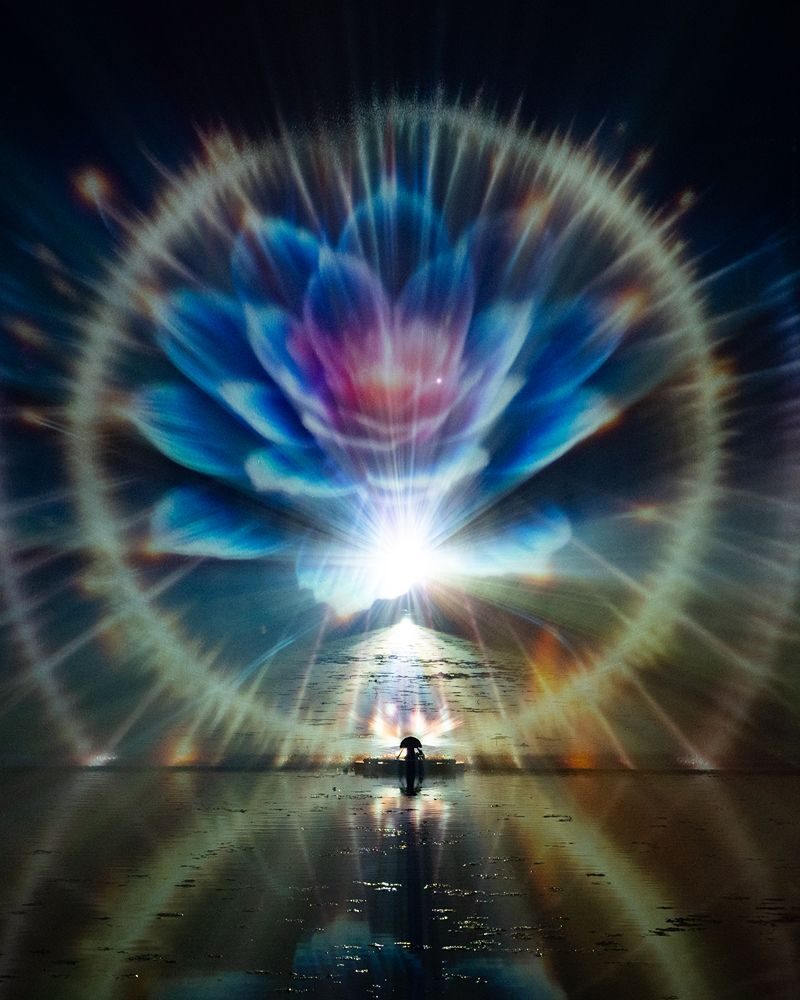 Large image of a blue, purple, pink Lotus flower in lights surrounded by two gold bands with a reflection on water.