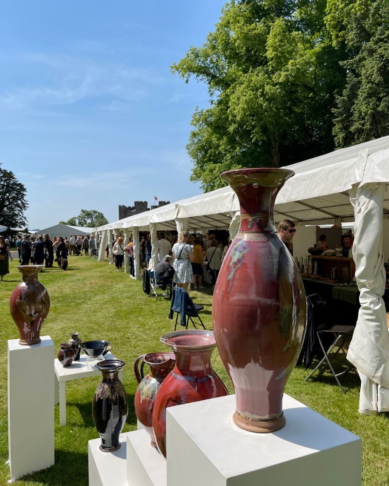 A variety of different large pots displayed on plinths overlooking a large grass area.