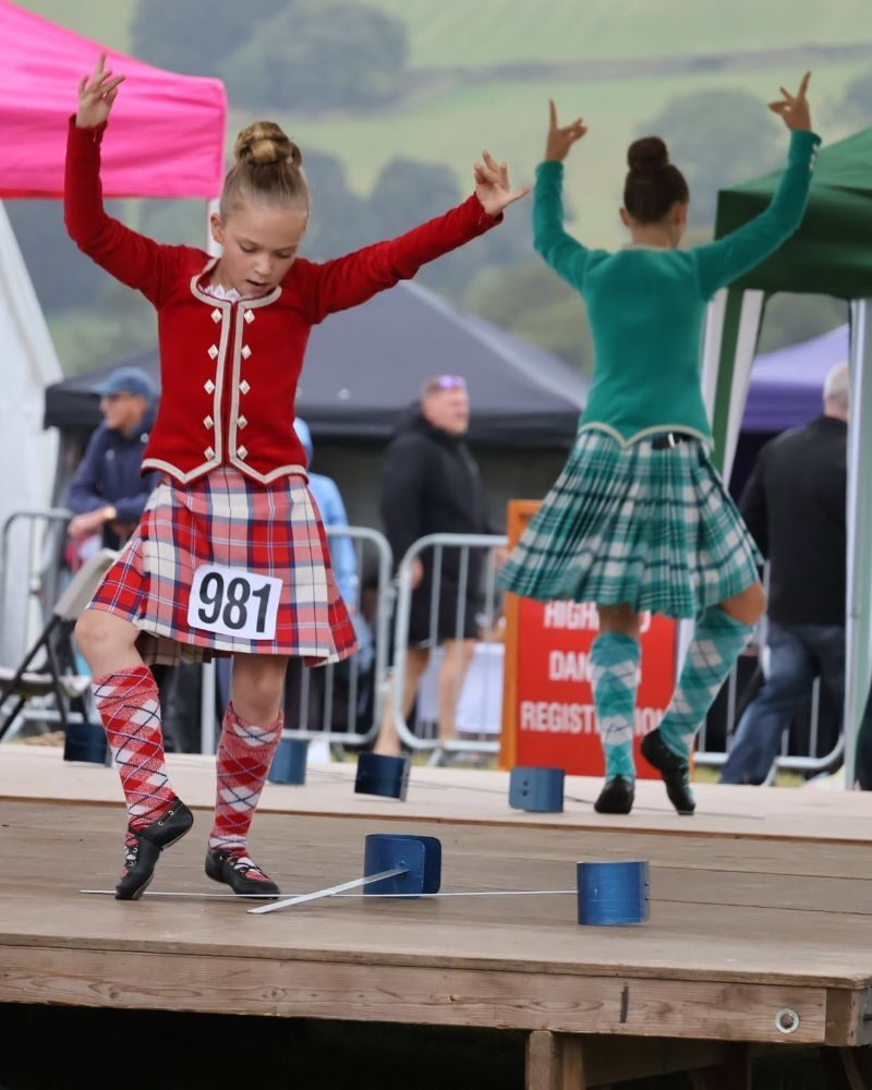 Two girls wearing tartan skirts highland dancing on a stage