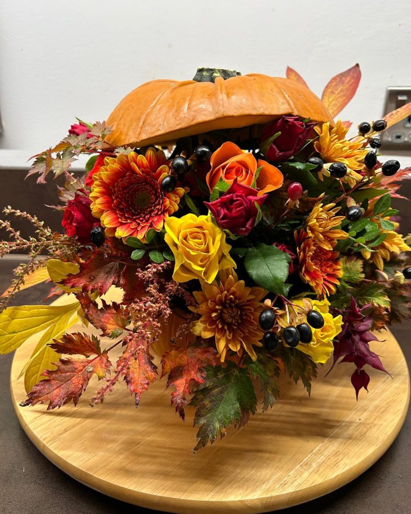 A pumpkin which is cut in half with an arrangement of orange and red flowers inside.