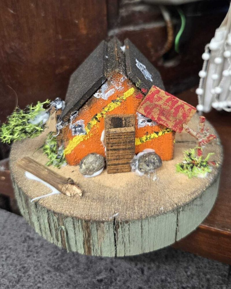 A handmade wooden orange haunted house with police tape around it sitting on a large wooden circle.