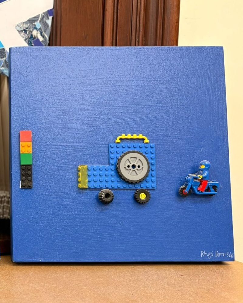 Blue canvas with a blue lego car and lego man on a blue motorcycle on it.