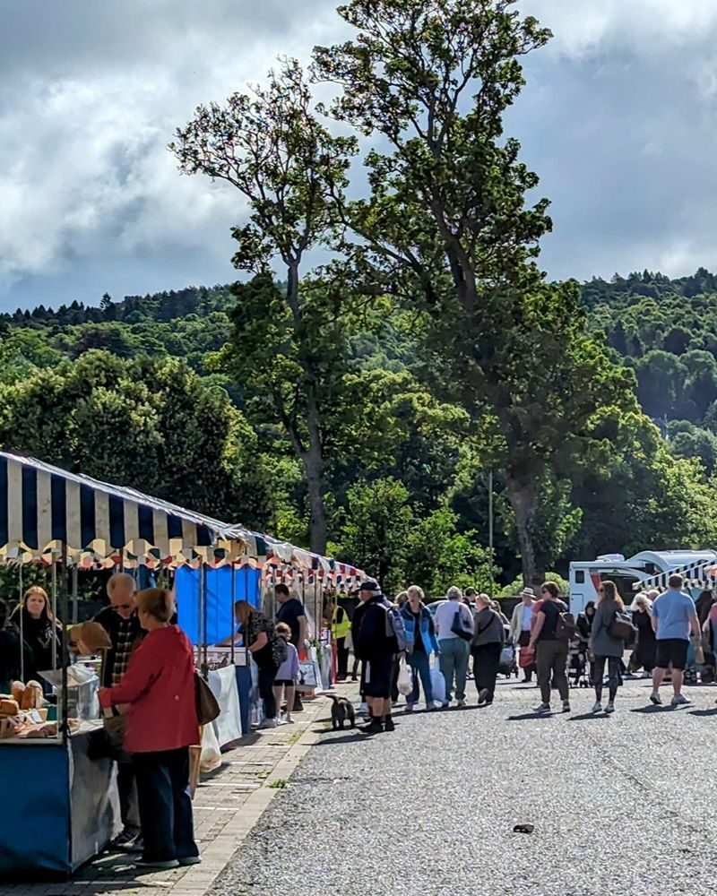 Brightly coloured market stalls with people browsing with green trees in background
