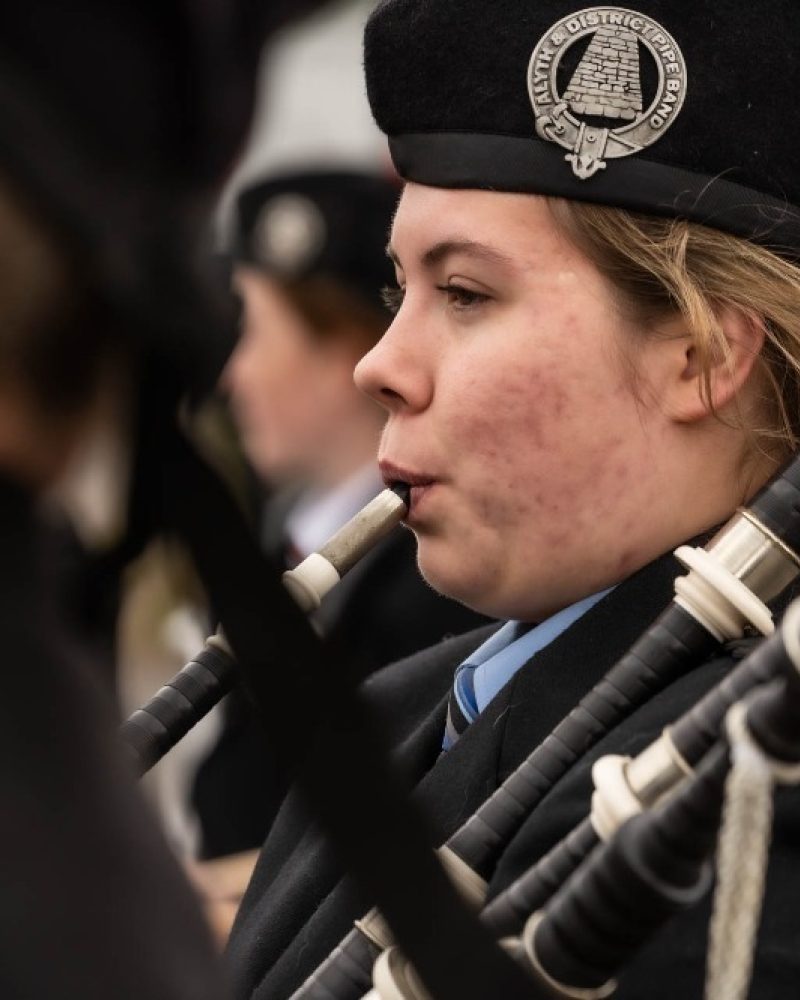 A woman playing the bagpipes wearing a blue shirt and a black jacket