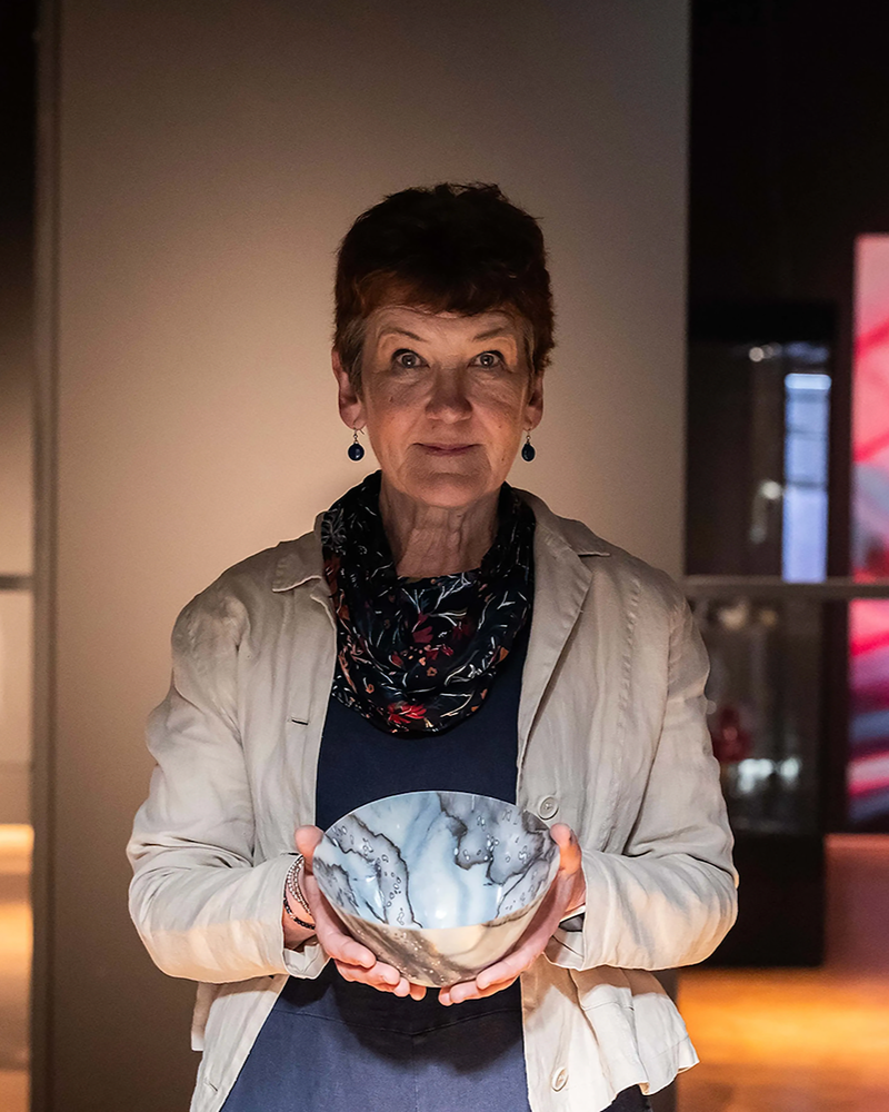 Short haired woman, in a open plan room , holding a handmade ceramic bowl.