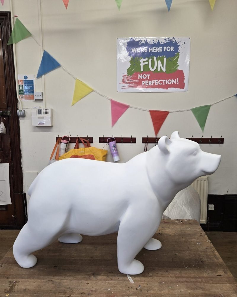 A white ceramic bear sitting on a wooden table.