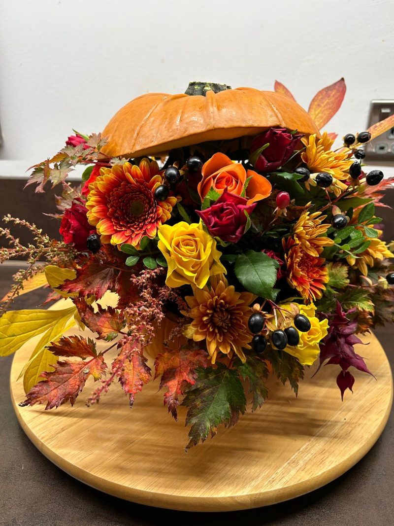 A pumpkin which is cut in half with an arrangement of orange and red flowers inside.