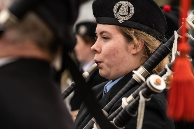 A woman playing the bagpipes wearing a blue shirt and a black jacket