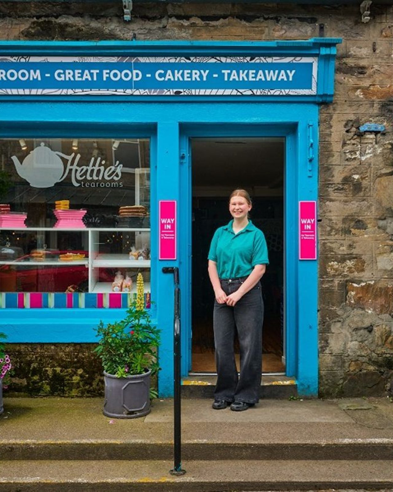 A smiling woman standing in front of the blue cafe.