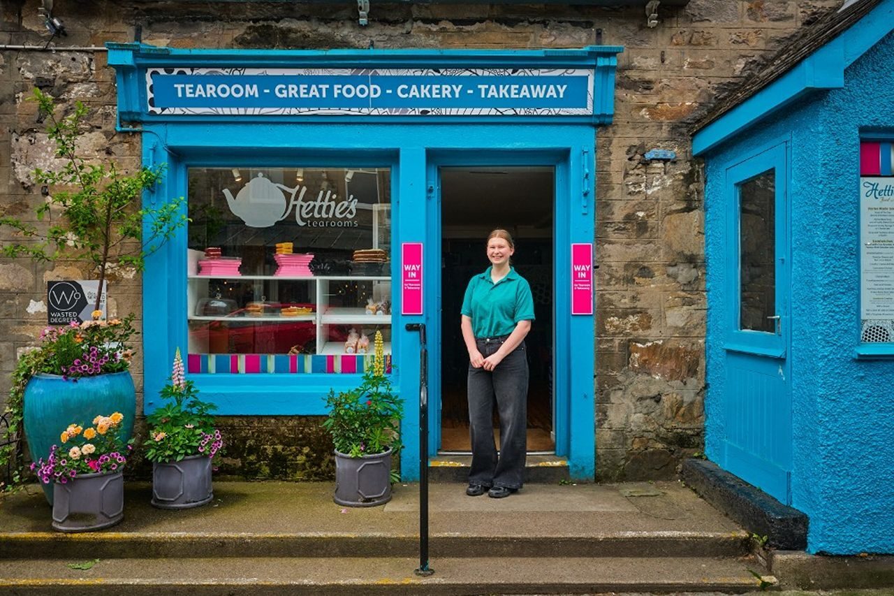 A smiling woman standing in front of the blue cafe.