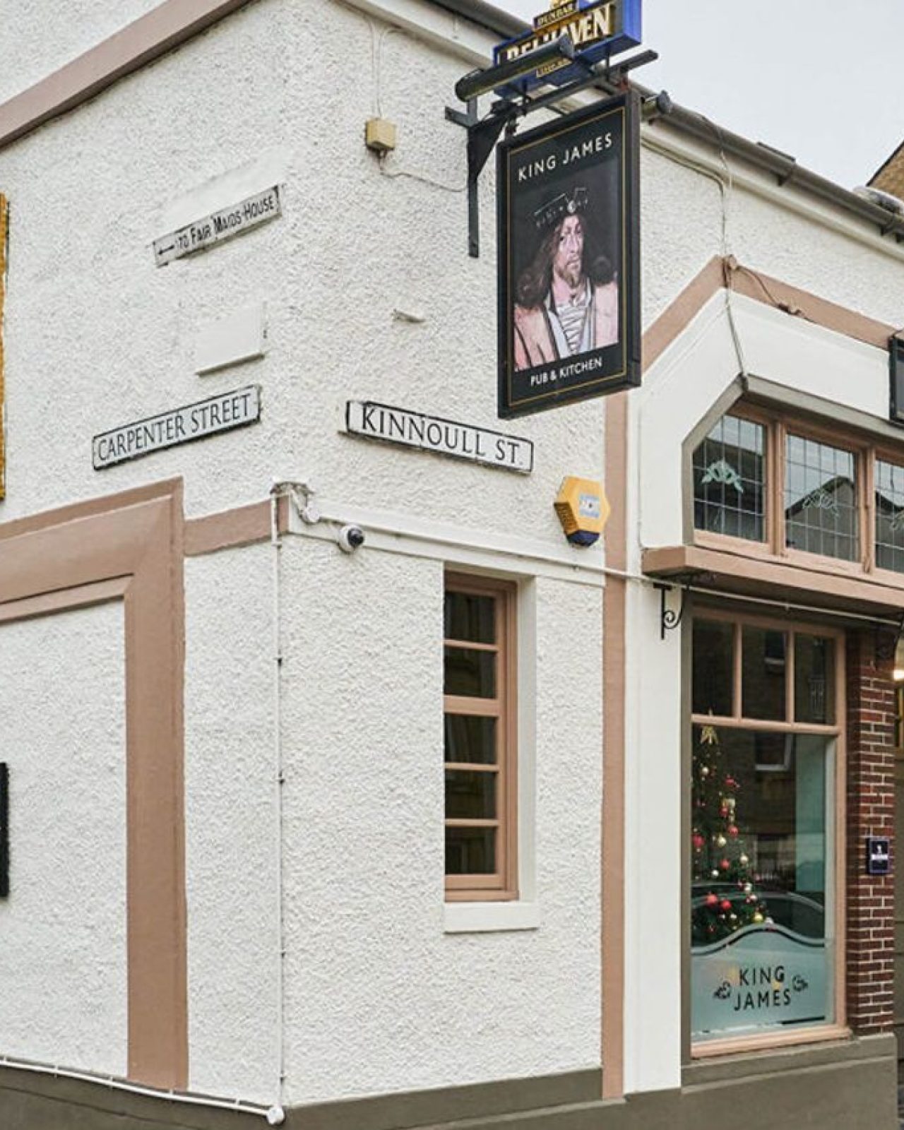 A white pub building in Perth with beige windows and a black sign with a portrait of Scottish King James