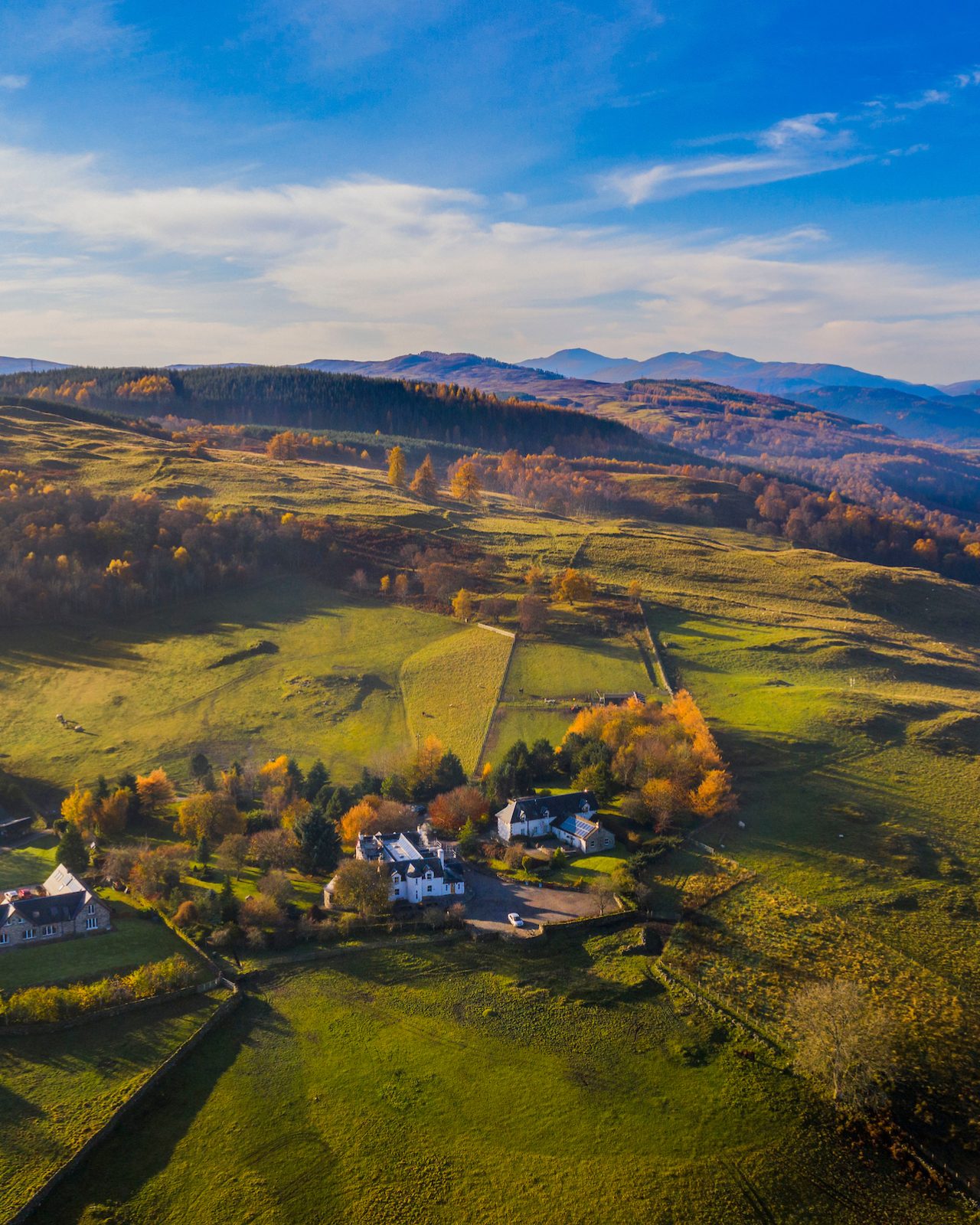 Three white old buildings set on a hilltop with green fields and mountains in the background on a sunny day