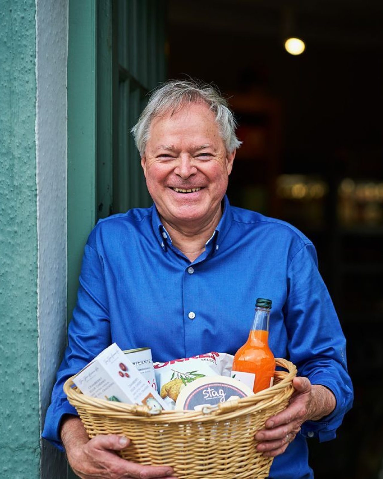 Smiling man in a blue shirt holding a basket with food and drink items from the Cornerstone Deli