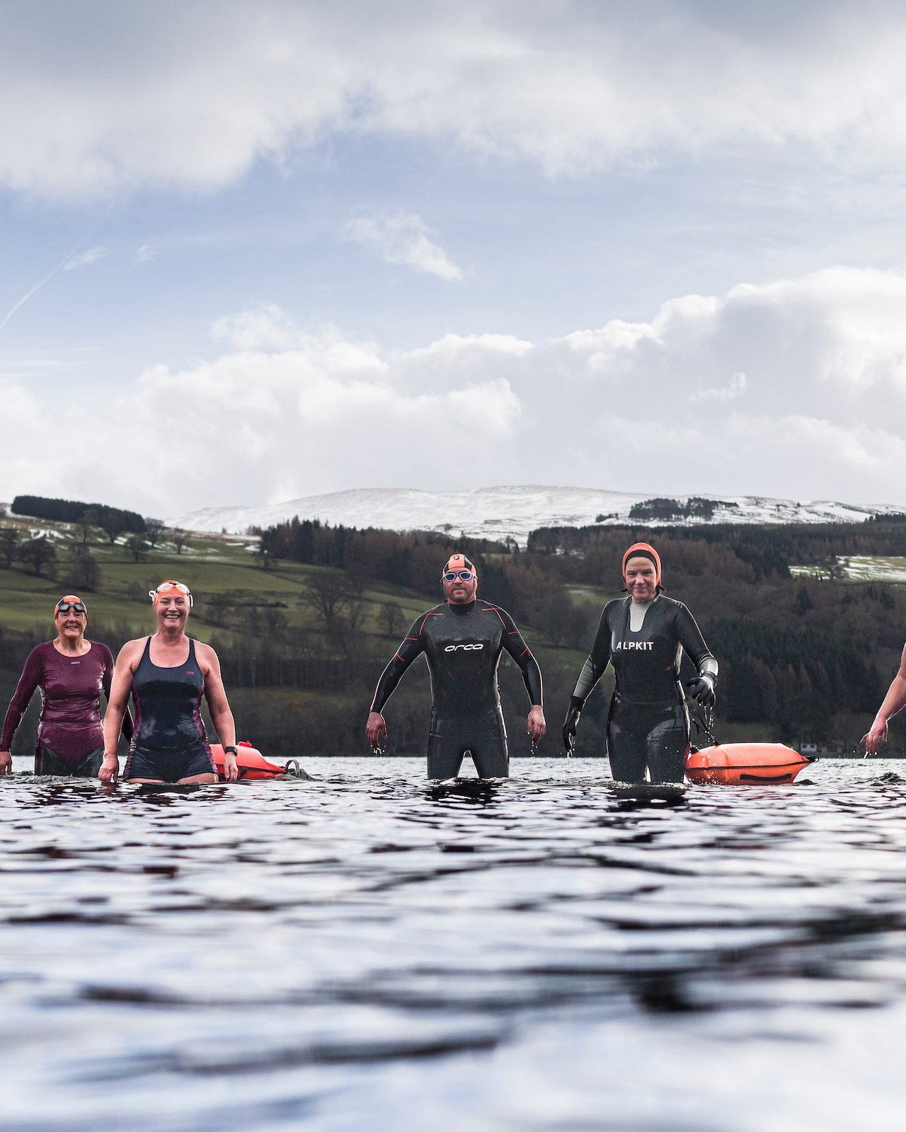 A group of people wearing swimwear standing knee deep in a loch looking very happy.