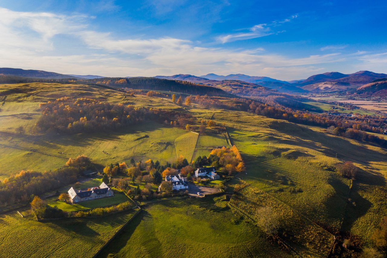 Three white old buildings set on a hilltop with green fields and mountains in the background on a sunny day
