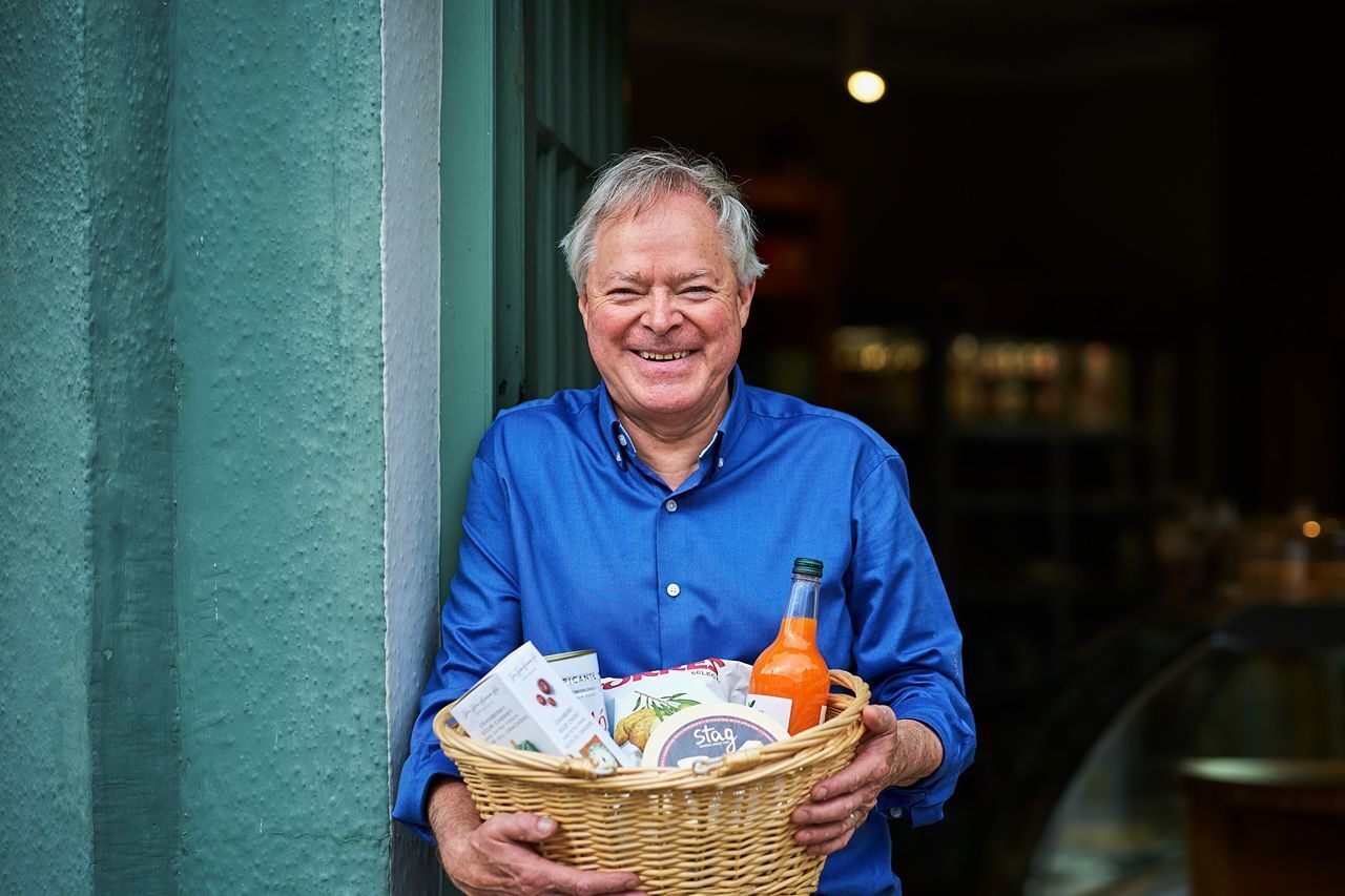 Smiling man in a blue shirt holding a basket with food and drink items from the Cornerstone Deli