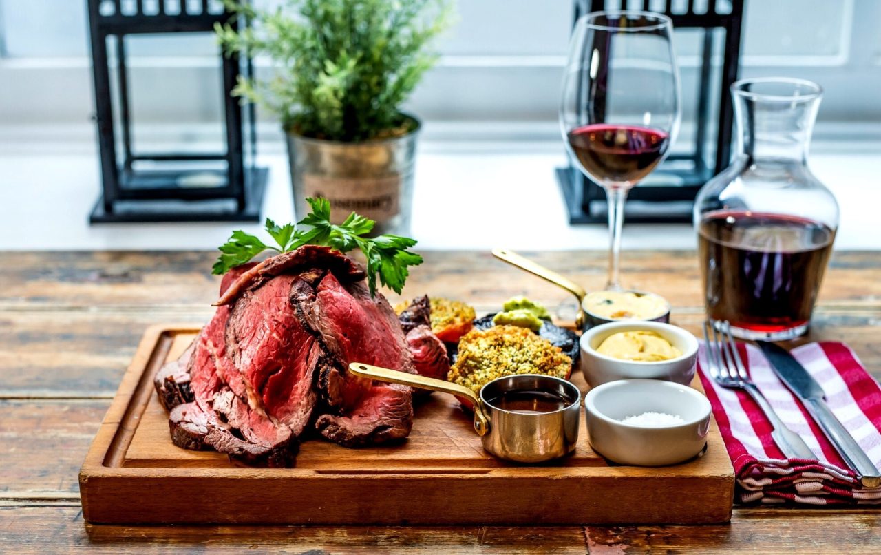 A platter of cooked meat, assorted condiments, and red wine