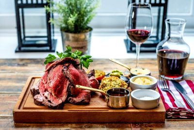 A platter of cooked meat, assorted condiments, and red wine