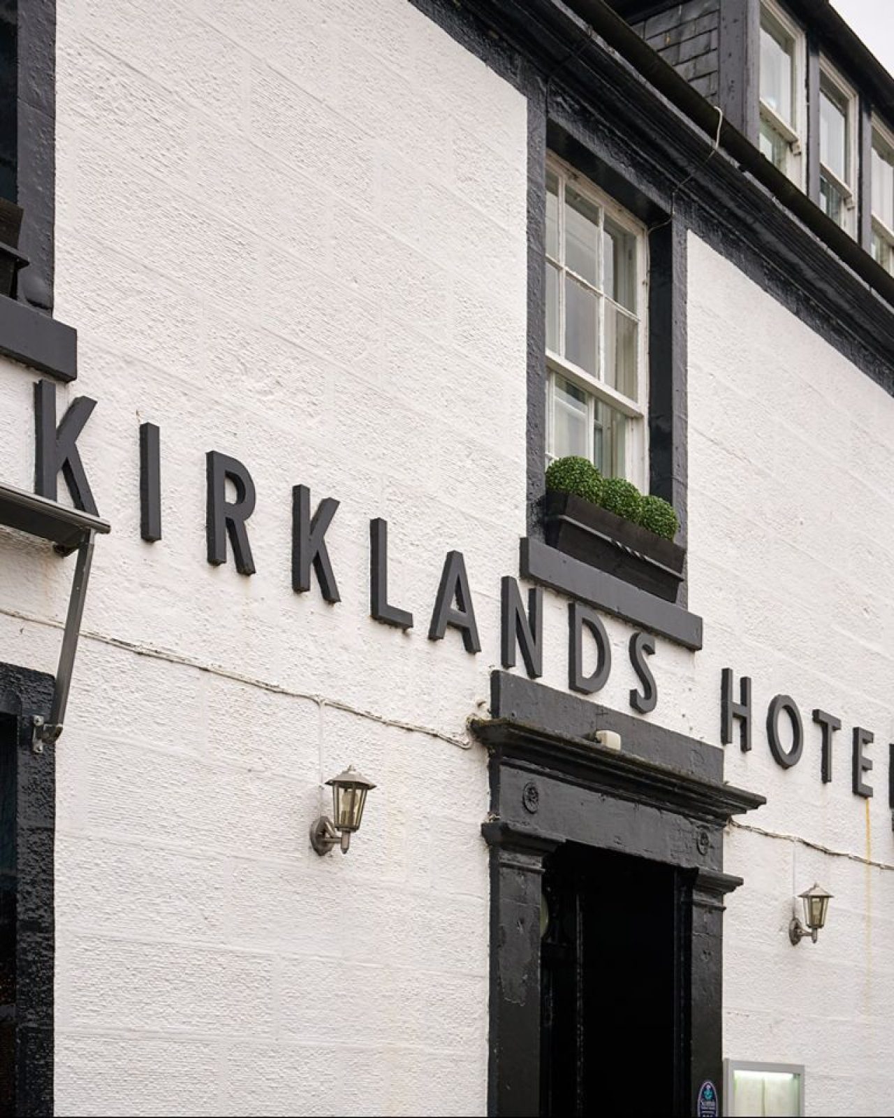 Black lettering sits in the middle of a white hotel building alongside black windows and a black door.