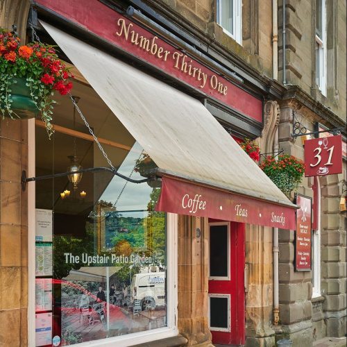 Number Thirty One has a large window partially covered by a beige and red canopy under a red sign and next to a red door.