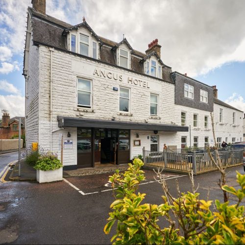 The Angus Hotel and Spa is white brick building with several windows and wooden door standing next to an outside patio
