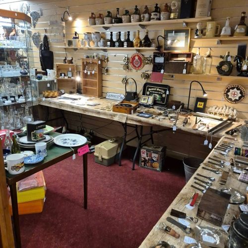 A cluttered room with a red carpet and beige walls containing shelves and tables covered in miscellaneous objects.