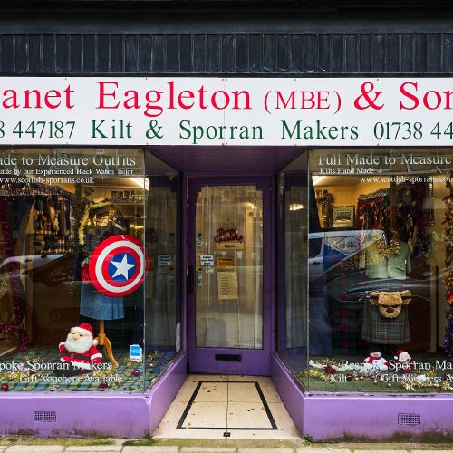 A purple shop with two large windows  display Scottish kilts and costumes, either side of a glass pane door